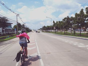 Rear view of boy riding bicycle on road in city