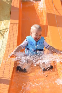 Full length of cheerful boy sliding on water slide