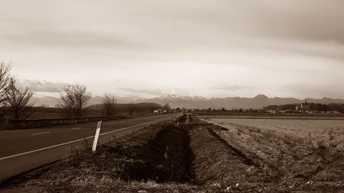 Empty road amidst field against sky