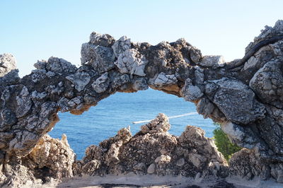 Stone arch at beach against sky