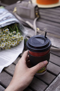 Cropped hand holding a take away coffee cup on wooden table outdoor