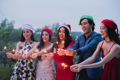 Smiling friends holding sparklers while standing in back yard during christmas