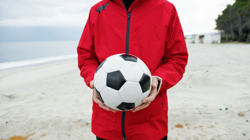 Midsection of man holding soccer ball at beach