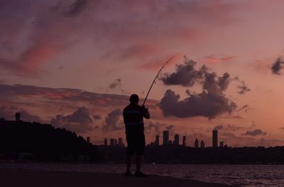 Man fishing by the sea against the sky during sunset