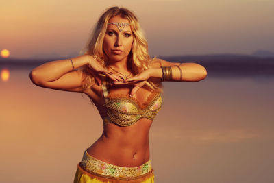 Portrait of beautiful woman standing at beach during sunset