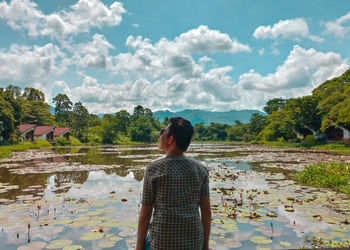 Rear view of man standing against pond