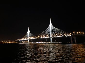 Illuminated bridge over river against sky at night