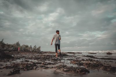 Man standing on shore by sea against sky