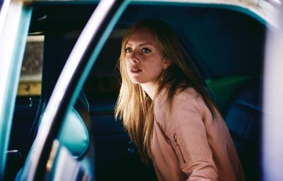 Side view of beautiful young woman sitting in car seen through window