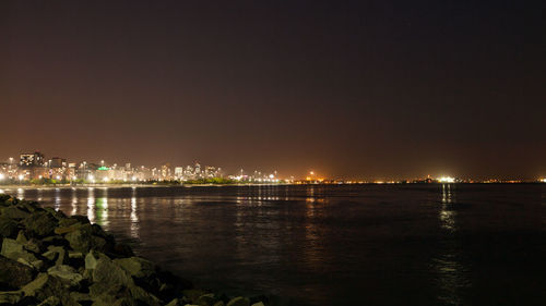 Illuminated city by river against sky at night