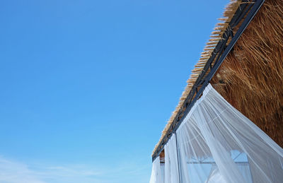 Edge roof is covered with dry palm leaves against the background blue sunny sky. 