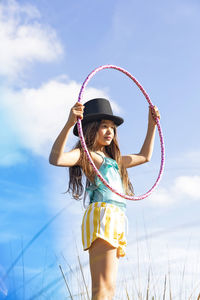 Girl wearing hat holding plastic hoop under sky