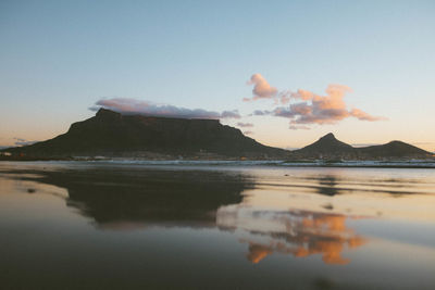 Scenic view of table mountain with reflection on wet shore against sky during sunset