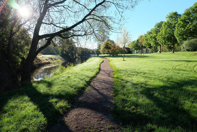 Footpath on grassy field by river against sky