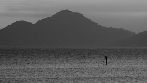 Silhouette man paddleboarding on lake against mountains