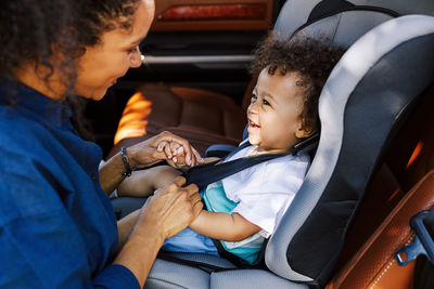 Smiling boy looking at mother tying seat belt