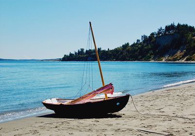 Boat moored on beach against clear blue sky