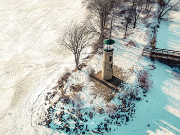 Snow covers the land and the icy surface of the lake surrounding the old lighthouse.