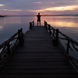 Silhouette man on pier over sea against sky during sunset