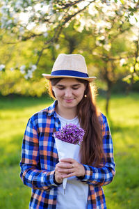 Girl holding a bouquet lilacs in the green garden on the sunset. shy young girl in hat