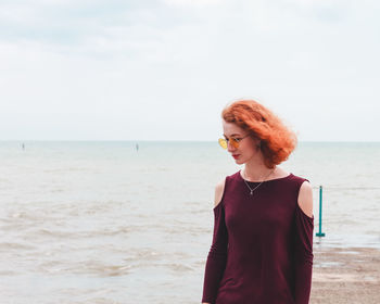 Young woman standing on pier by sea against sky