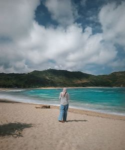 Rear view of woman walking at beach against cloudy sky