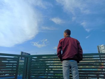 Rear view of man standing by railing against sky