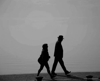 Silhouette people walking on shore against sky