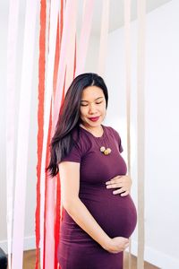 Smiling pregnant woman with hands on stomach standing at home