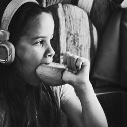Side view of girl with food in mouth wearing headphones at home