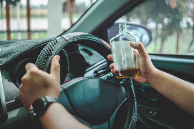 Hand of man driving car by holding alcohol bottle