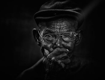 Close-up portrait of senior man covering mouth against black background