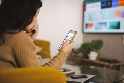 Woman controlling tv through smart phone at home