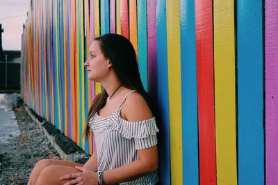 Thoughtful young woman sitting against colorful wooden fence