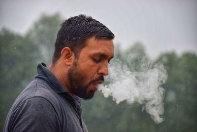 Side view of man smoking against trees