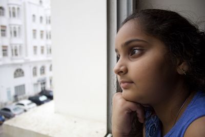 Close-up portrait of girl looking away through window