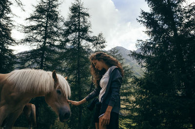 Side view of young woman standing by tree against sky