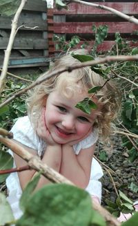 Portrait of cute smiling girl with hands on chin sitting in park