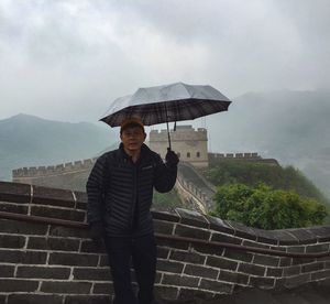 Portrait of man with umbrella standing on steps at great wall of china
