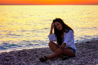 Young woman sitting on shore at beach during sunset