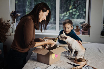 Happy family mom and kid putting bone in pet subscription box for dogs. chihuahua dog and