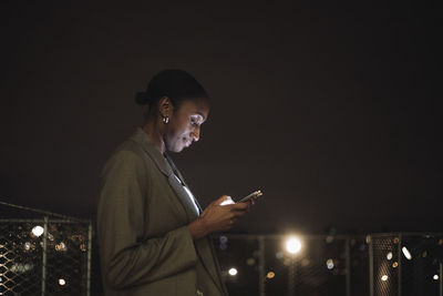 Side view of businesswoman text messaging on mobile phone at night