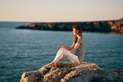 Man sitting on rock by sea against sky