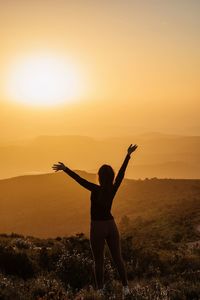 Rear view of man standing on mountain at sunset