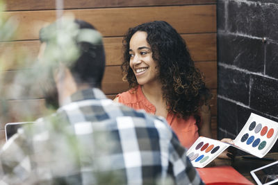 Woman smiling while sitting with male coworker in office