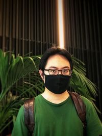 Portrait of young man standing indoors against plants, textured wall and neon lighting.