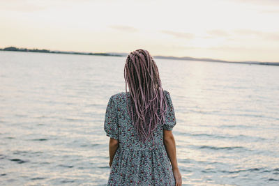 Rear view of woman standing by sea against sky