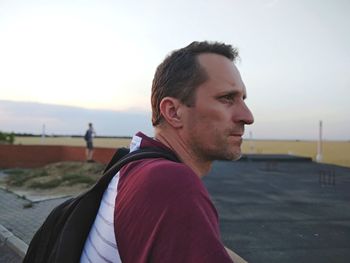 Side view of man with backpack looking away against clear sky