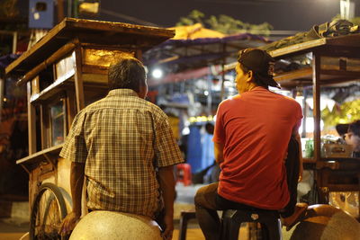 Rear view of vendors sitting outdoors at night