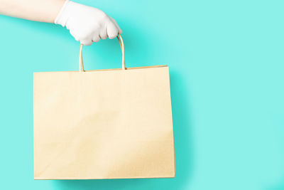 Hand in a glove holds a paper bag on a blue background close-up.